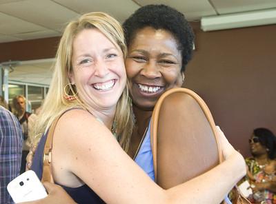 two female alumni embrace for a hug and look straight ahead and smile for the camera