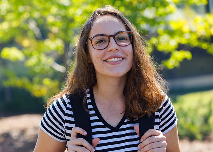 brunette female wearing black and white horizontal striped shirt with dark rim glasses smiling at the camera, yellow leaves in the background