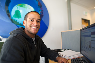 student sitting at computer, smiling at camers, painting of earth in background
