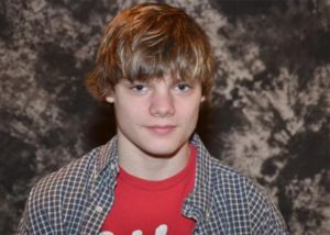 A young man with blonde hair, smiling, looking at camera.