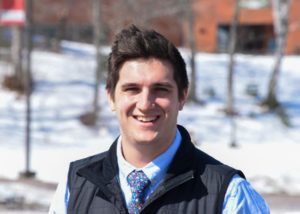 A man with dark hair, smiling, with snow in background.