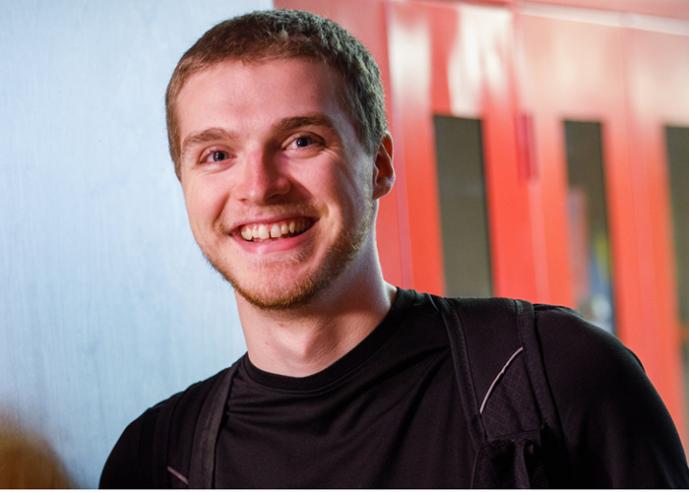 A young man in a black t shirt, smiling, looking at camera.