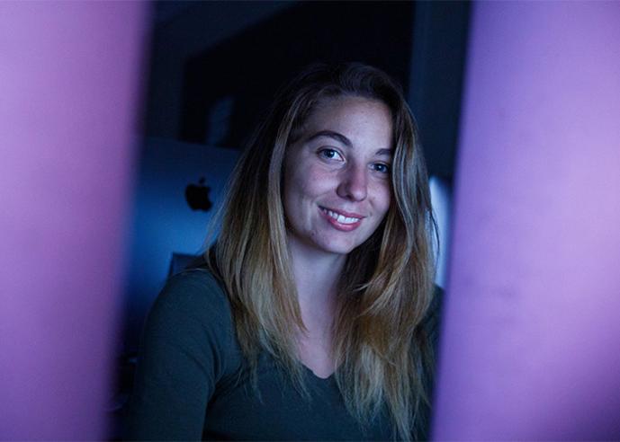 A female student sitting at a desk with a computer, smiling, looking at camera.