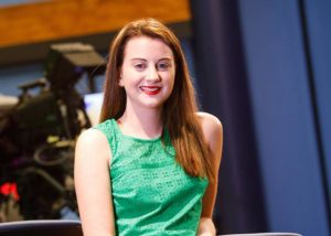 A young lady wearing a green dress with red hair, smiling, looking at camera.