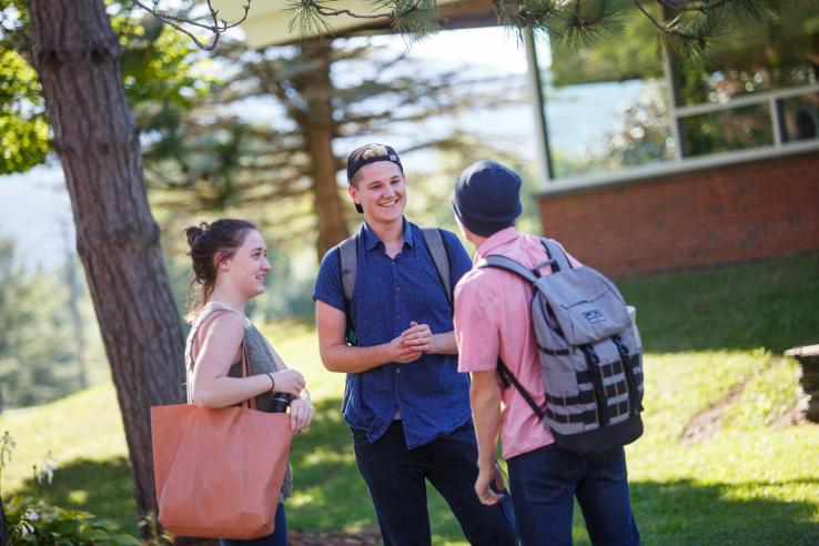 Three students stop and talk to one another outside a college campus building.