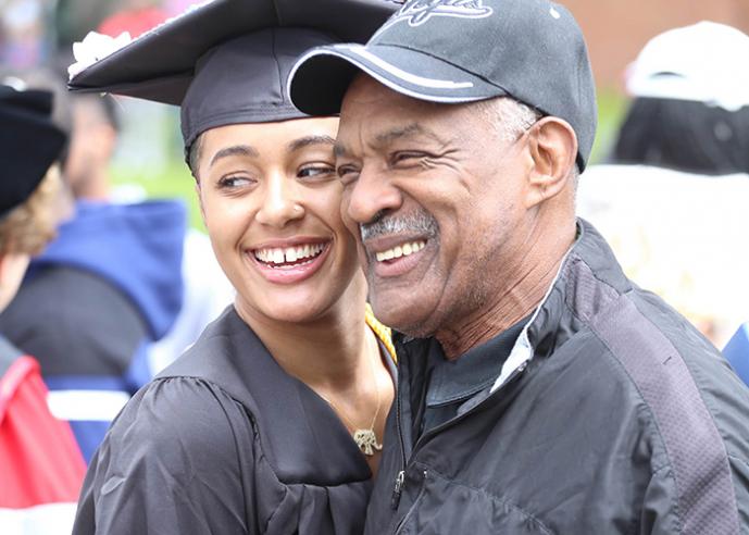 A father and daughter pose for a photo at a graduation ceremony, smiling.