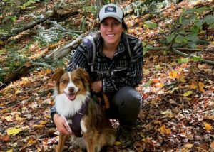 A woman smiling with her dog, autumn leaves in background.