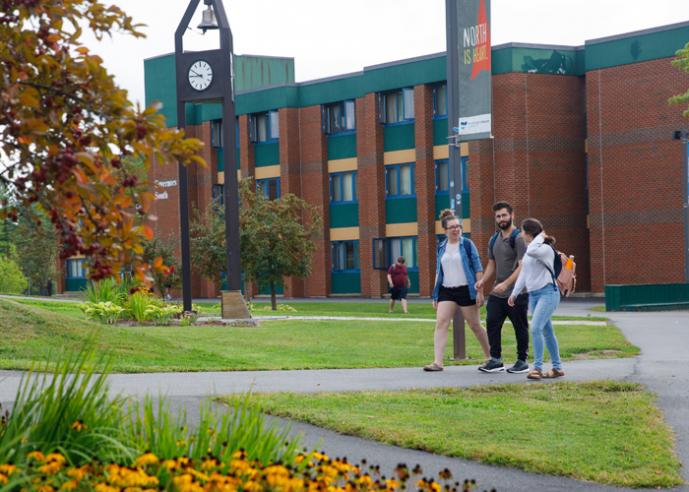 Students walking outside of a college campus building, with yellow flowers in foreground.
