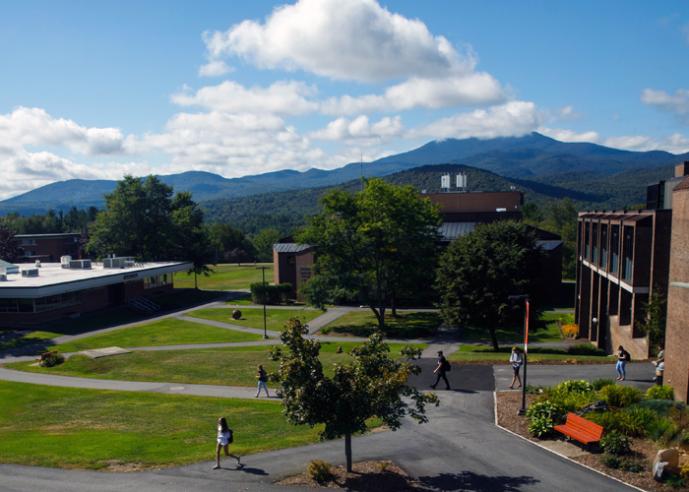 Students walking outside of college campus buildings, with mountains and trees in background.