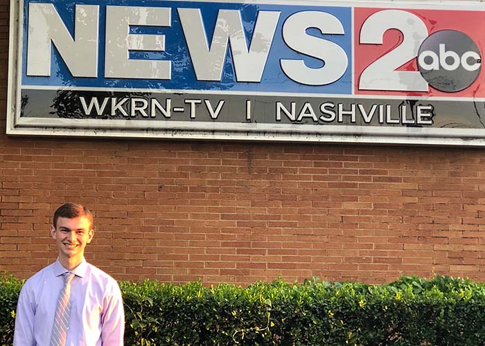 A young brown haired man standing in front of a News 2 ABC sign.