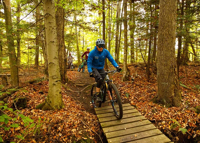 A young man in a blue jacket and helmet riding a mountain bike onto a wooden bridge.