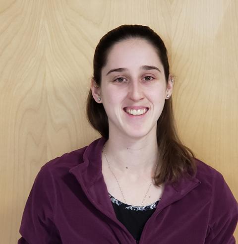 A young woman with long, brown hair, smiling, looking at the camera.