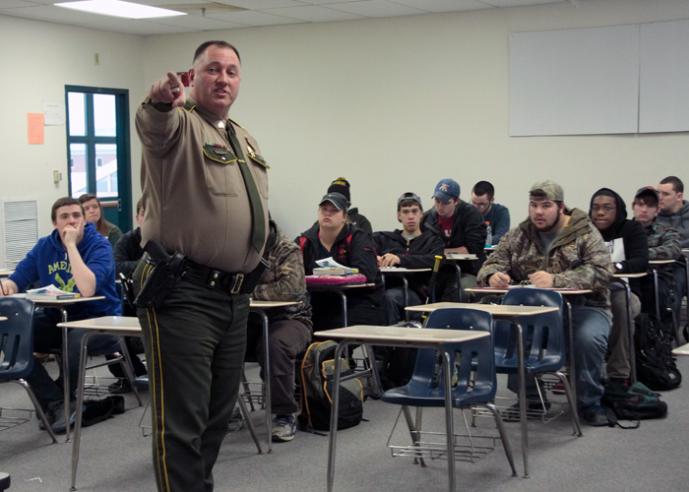 A police officer speaks to a group of students in a classroom.