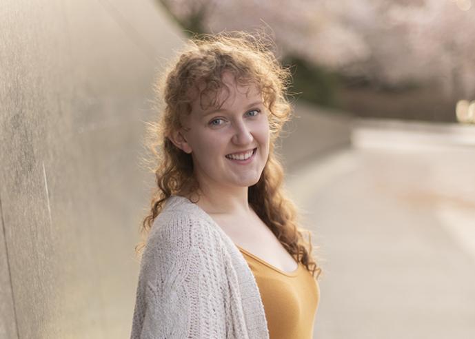 A young woman with long, curly hair, smiling, looking at camera.