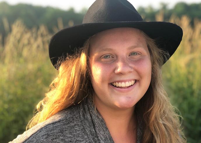 A young woman wearing a black hat, smiling, looking at camera.