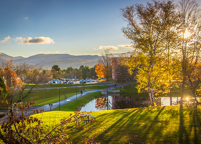 An outdoor view of a college campus at sunrise, with pond in foreground.