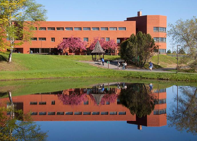 A college campus building with a pond in the foreground and blue sky in background.