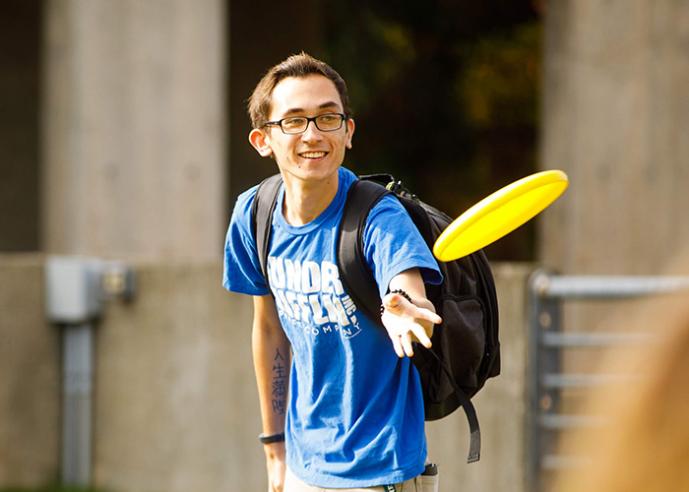 A young man wearing a blue t shirt, throwing a yellow frisbee.