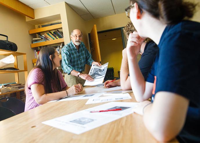 A male teacher is showing a group of students a newspaper page.