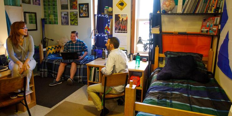 A female and two male students hang out in a dorm room.