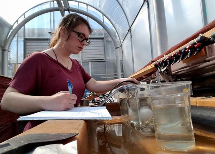 A female student wearing glasses takes notes on an experiment in a Biology lab.