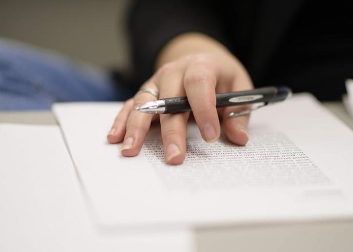 A woman's hand holding a black pen, on top of a paper with typed words.