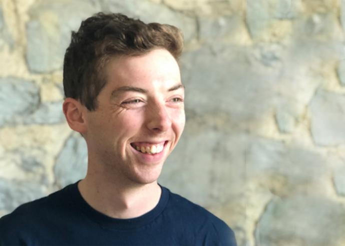 A young man wearing a black t shirt, smiling, looking off to his left side.