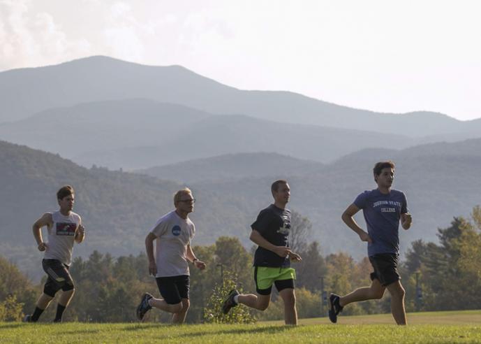 Four men jogging outdoors, hills and trees in background.