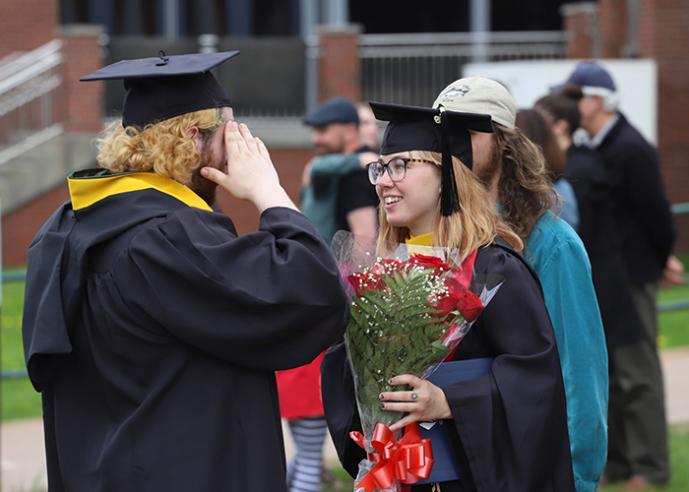 Two graduates wearing caps and gowns talk at a graduation ceremony.