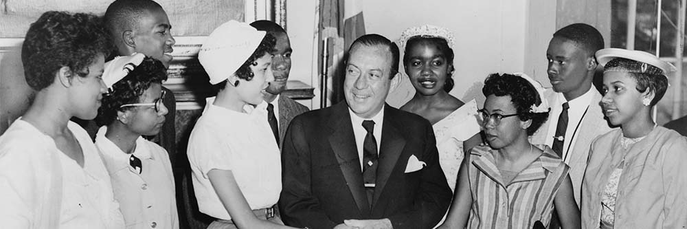 A group of young black student standing around a balding white man in a suit.
