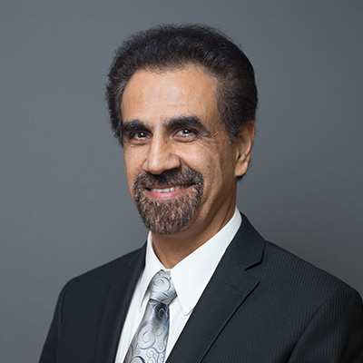 A main with dark hair and a goatee smiles at the camera while wearing a suit and tie.