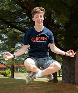 A young boy seems to be hovering in the air in a meditation positions, he smiles at the camera.