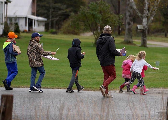 A group of one adult and numerous children are walking outside in the rain away from the camera.