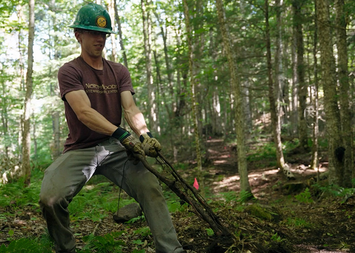 A young man with a green helmet is pulling really hard against a root in the ground.